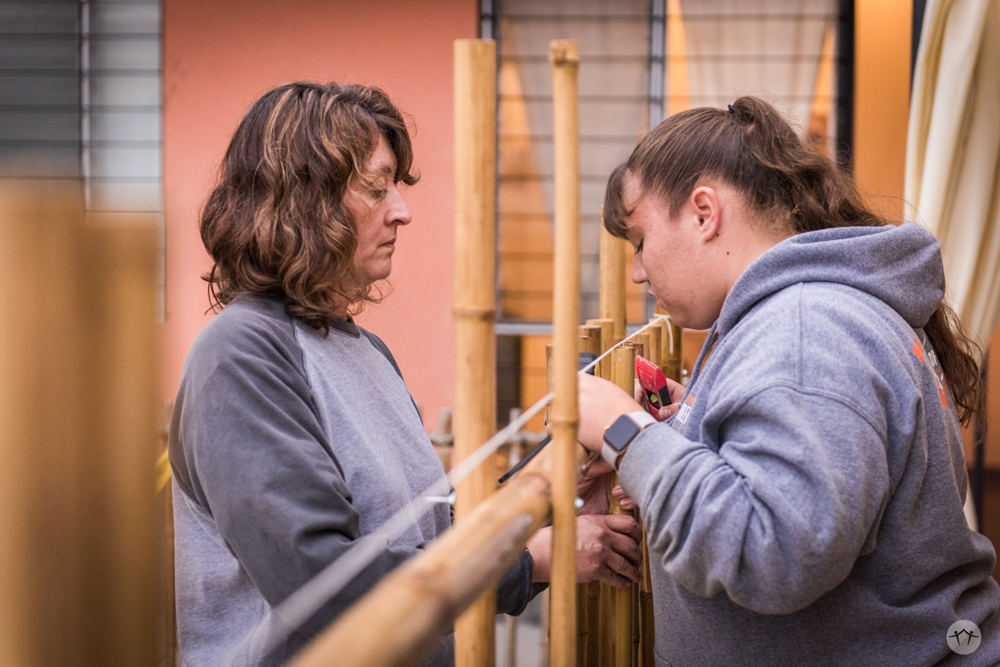 Two of the team members attaching vertical poles to the bamboo fence