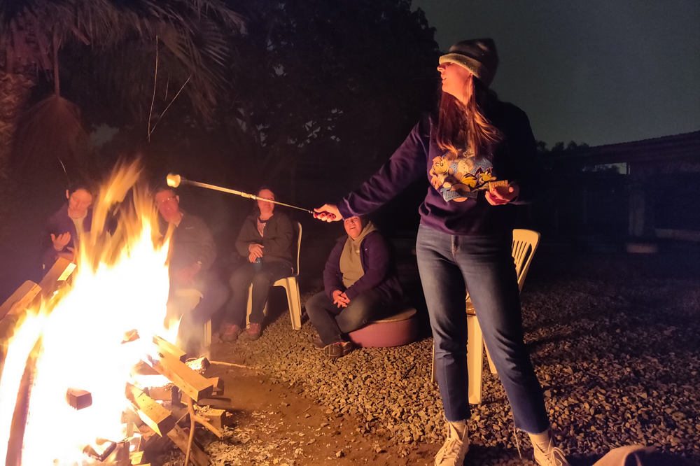 Julie toasting a marshmallow with her hat pulled over her eyes